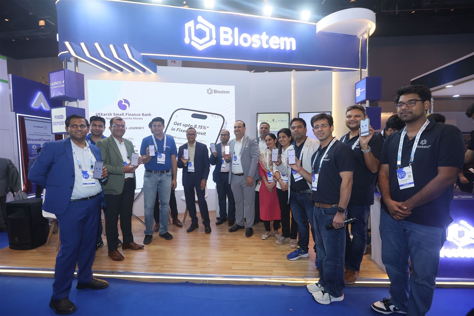 The Blostem team and partners holding up phones with the MobiKwik app at the launch of Utkarsh Small Finance Bank FDs on MobiKwik